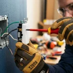 Elektrikář provádějící bezpečnou výměnu nástěnného vypínače osvětlení pomocí izolovaného šroubováku